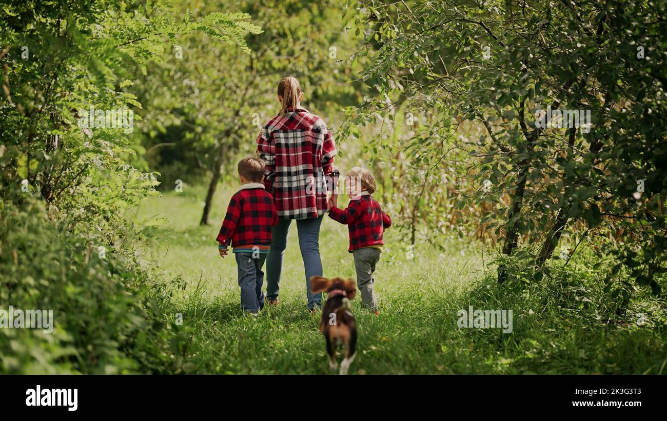 Junge Familie - Mutter und zwei Brüder Zwillinge Jungen läuft mit Welpen Beagle Hund im grünen Park oder Garten. Glückliche Mutter und Kinder, Liebe, Freiheit, Zukunft Stockfoto