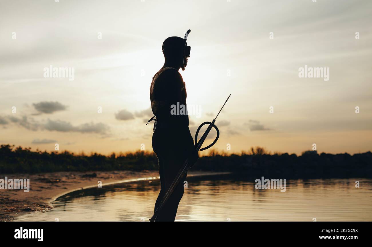 Seitenansicht des Speerfischers, der am Ufer des Meeres steht und ins Meer blickt. Männlicher Taucher geht Speerfischen mit einer Speergun. Stockfoto