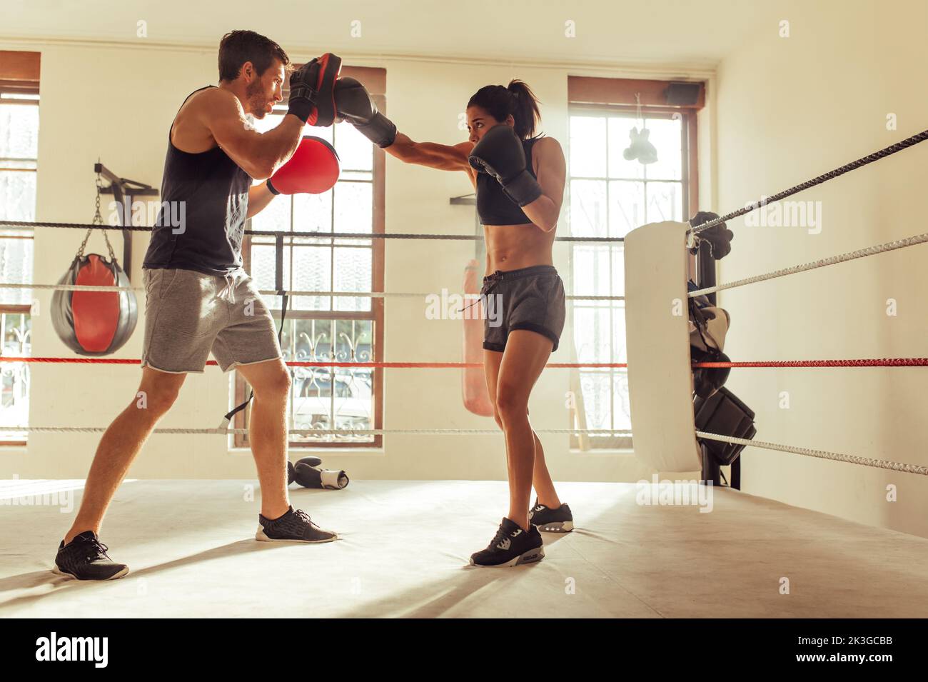 Männlicher Trainer hilft einer jungen Boxerin mit umgekehrten Schlägen in einem Boxring. Boxtrainer trainiert eine sportliche junge Frau im Fitnessstudio. Stockfoto