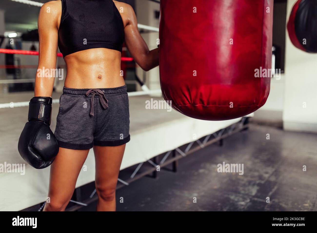 Junge Boxerin, die neben einem Boxsack in einem Fitnessstudio steht. Nicht erkennbare junge Frau in Sportkleidung und Boxhandschuhen im Fitnessstudio. Stockfoto