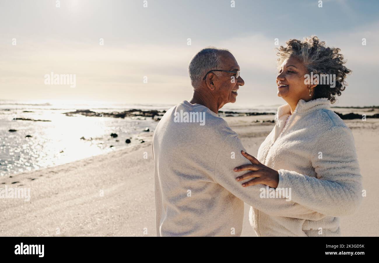 Reifes Paar lächelt und tanzt zusammen auf Strandsand. Ein glückliches älteres Paar, das sich am Meer gut Vergnügen hat. Fröhliches Seniorenpaar, das es genießt Stockfoto