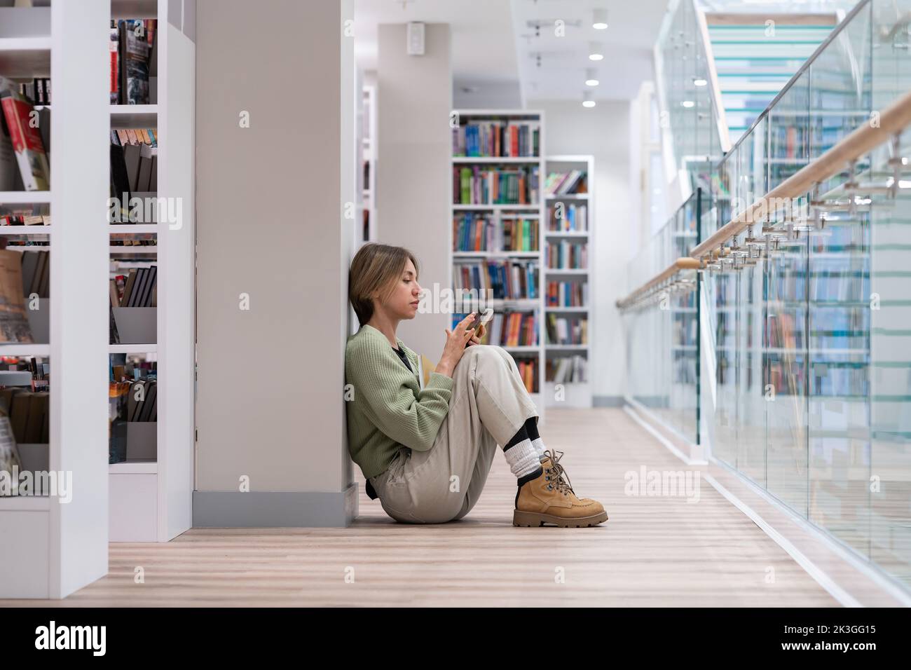 Studentin mittleren Alters, die auf dem Boden sitzt und in der Universitätsbibliothek ein Buch liest. Zweiter Grad. Stockfoto