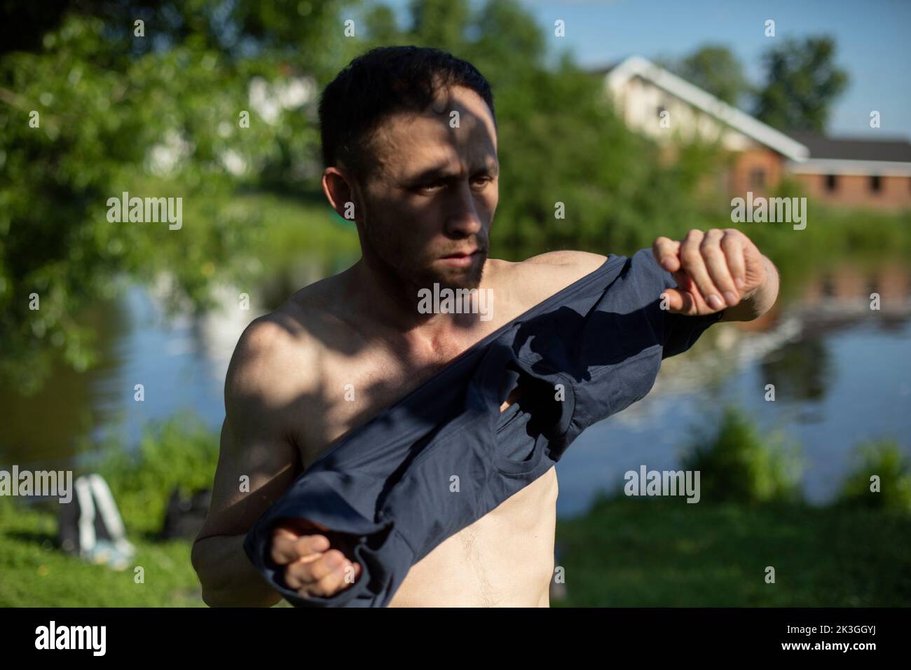 Mann am Strand im Sommer. Der Mensch bereitet sich auf das Schwimmen im See vor. Guy zog sein T-Shirt aus. Sonnenbaden im Sommer. Stockfoto