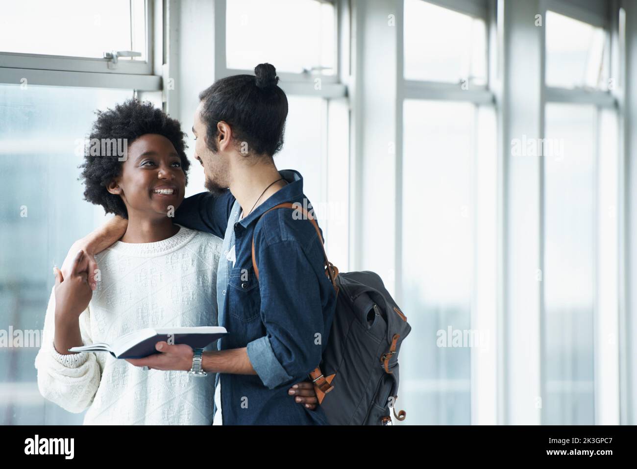 Beste Freunde. Ein studentisches Paar, das in den Universitätshallen steht und zusammen ein Lehrbuch anschaut. Stockfoto
