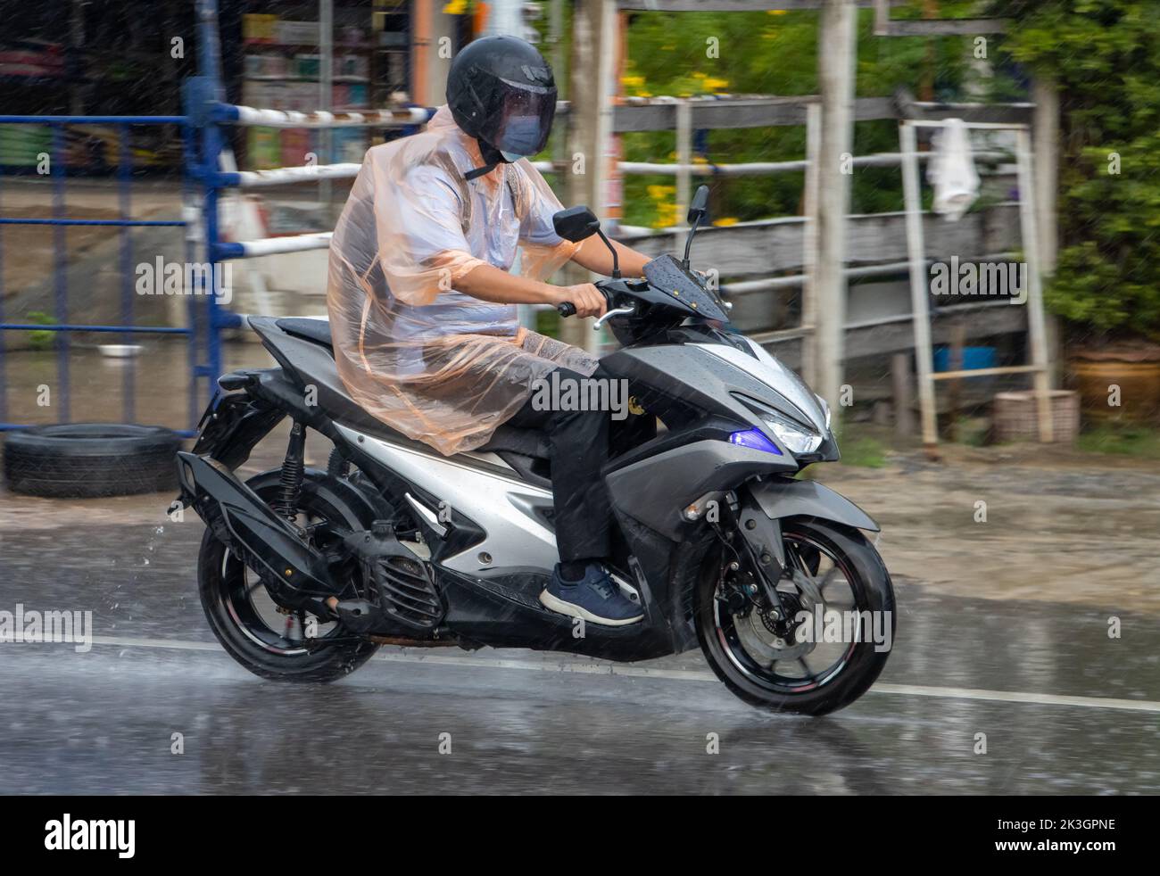 Ein Mann im Regenmantel fährt bei starkem Regen mit dem Motorrad auf die Straße Stockfoto