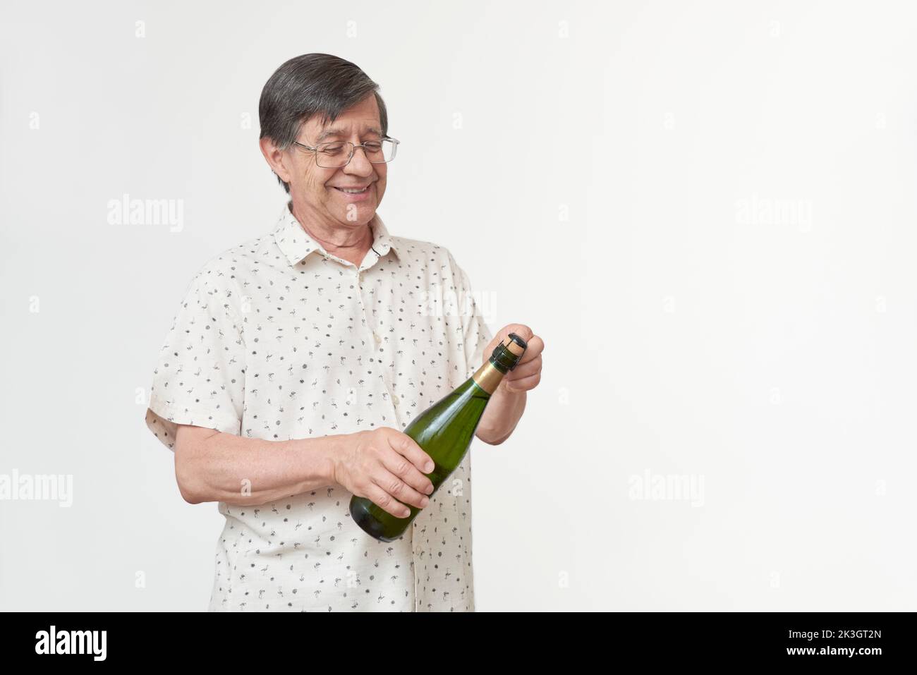 Hispanischer Senior lächelt, während er eine Flasche Champagner oder Apfelwein und ein paar Gläser in der Hand hält. Konzept des feierlichen Toasts. Stockfoto