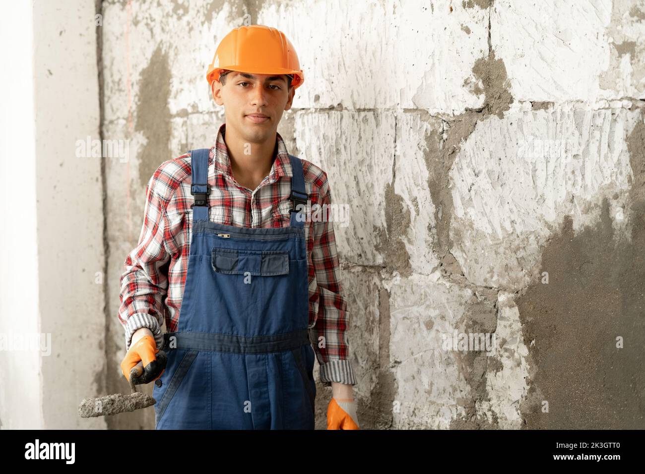 Muslimischer Baumeister mit Kelle und Zementmörtel auf weißem Backsteinwand-Hintergrund, Hausrenovierung und Umbaukonzept Stockfoto