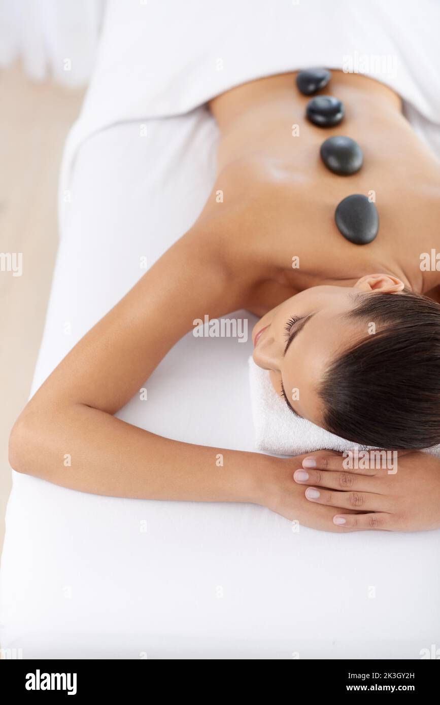 Massage mit heißen Steinen. Eine schöne junge Frau, die sich während der Spa-Behandlung entspannt. Stockfoto