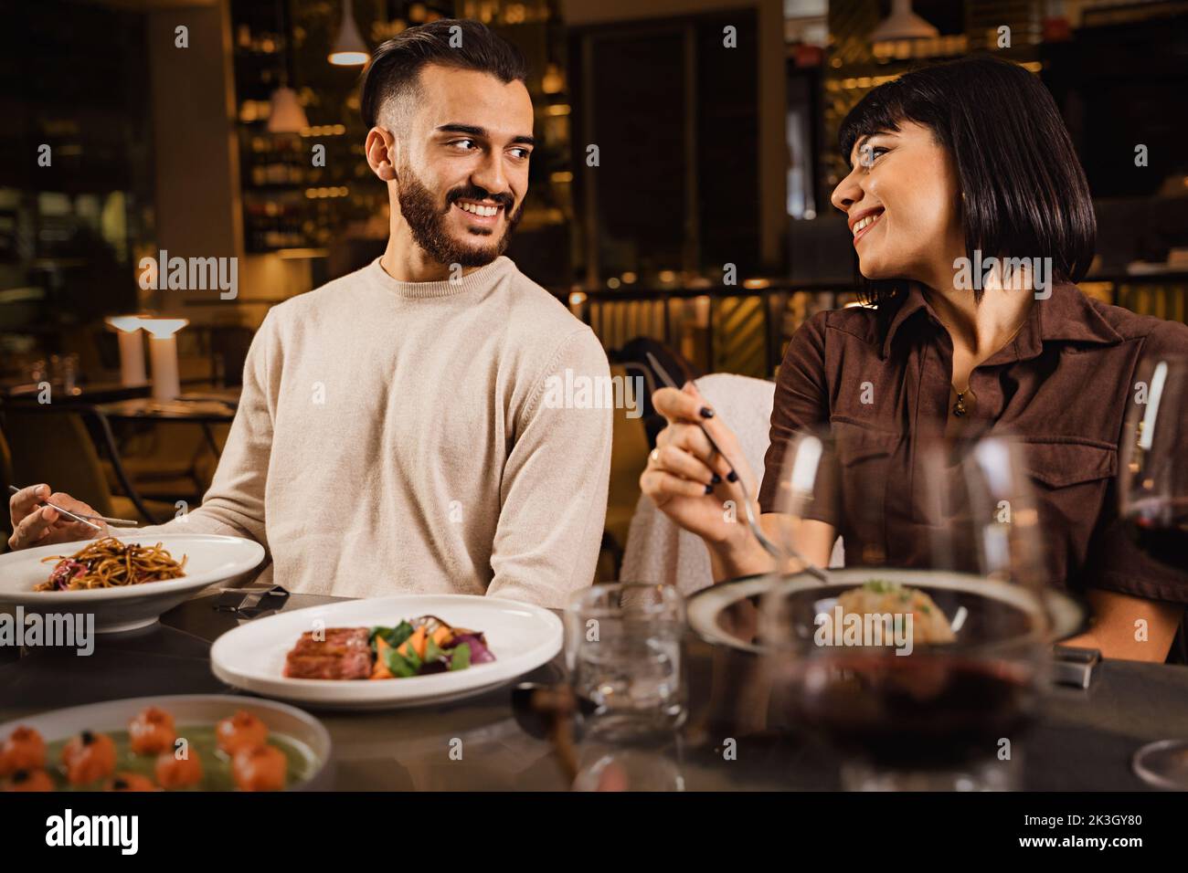 Ein glückliches Paar, das im Restaurant zu Abend gegessen hat und sich gegenseitig beobachtet hat - ein Paar, das sich an einem Date mit den Augen in Verbindung gesetzt hat und abends im Luxusrestaurant gegessen hat Stockfoto