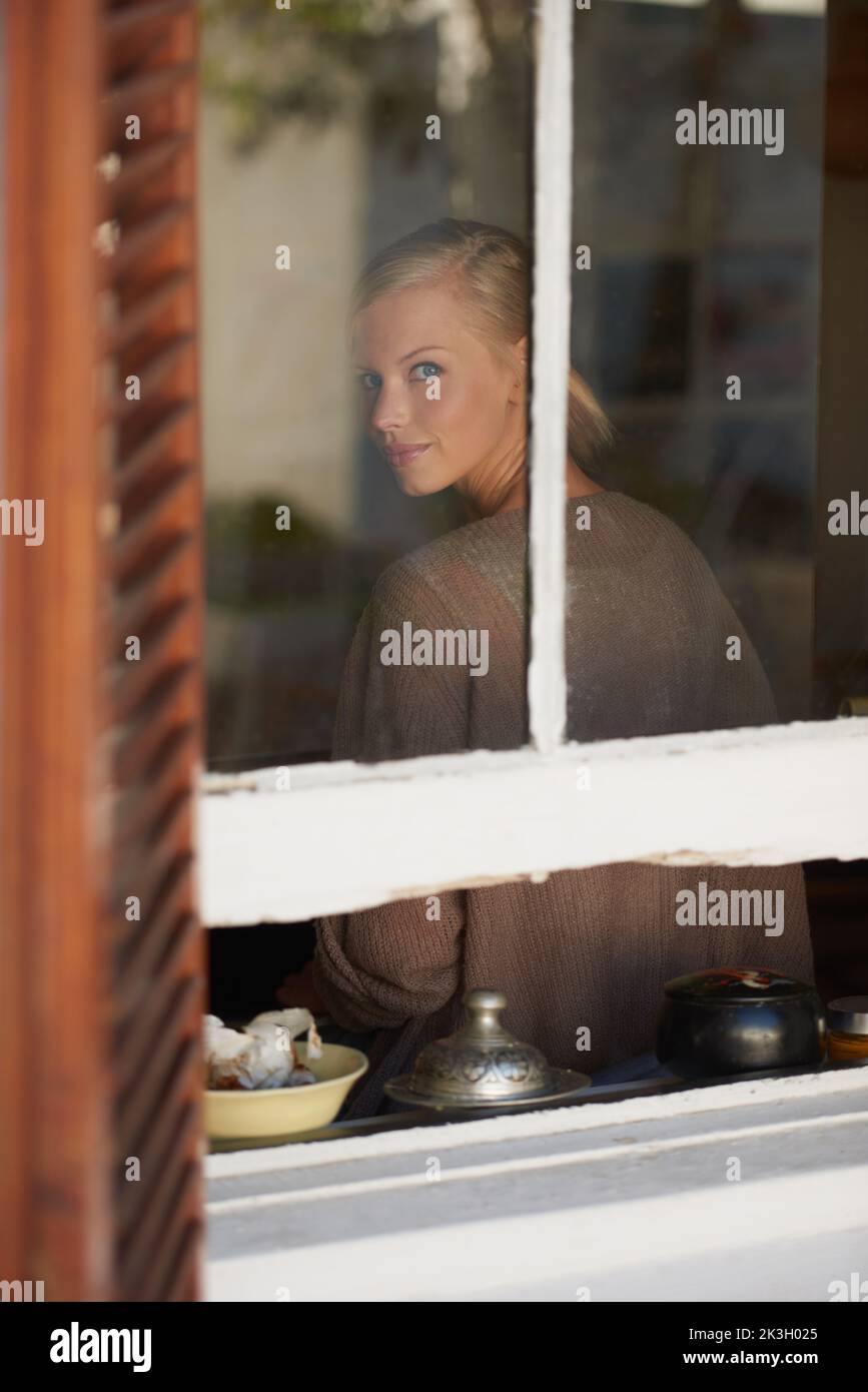 In einer friedlichen Geisteshaltung. Eine junge Frau, die durch ihr Fenster schaut. Stockfoto