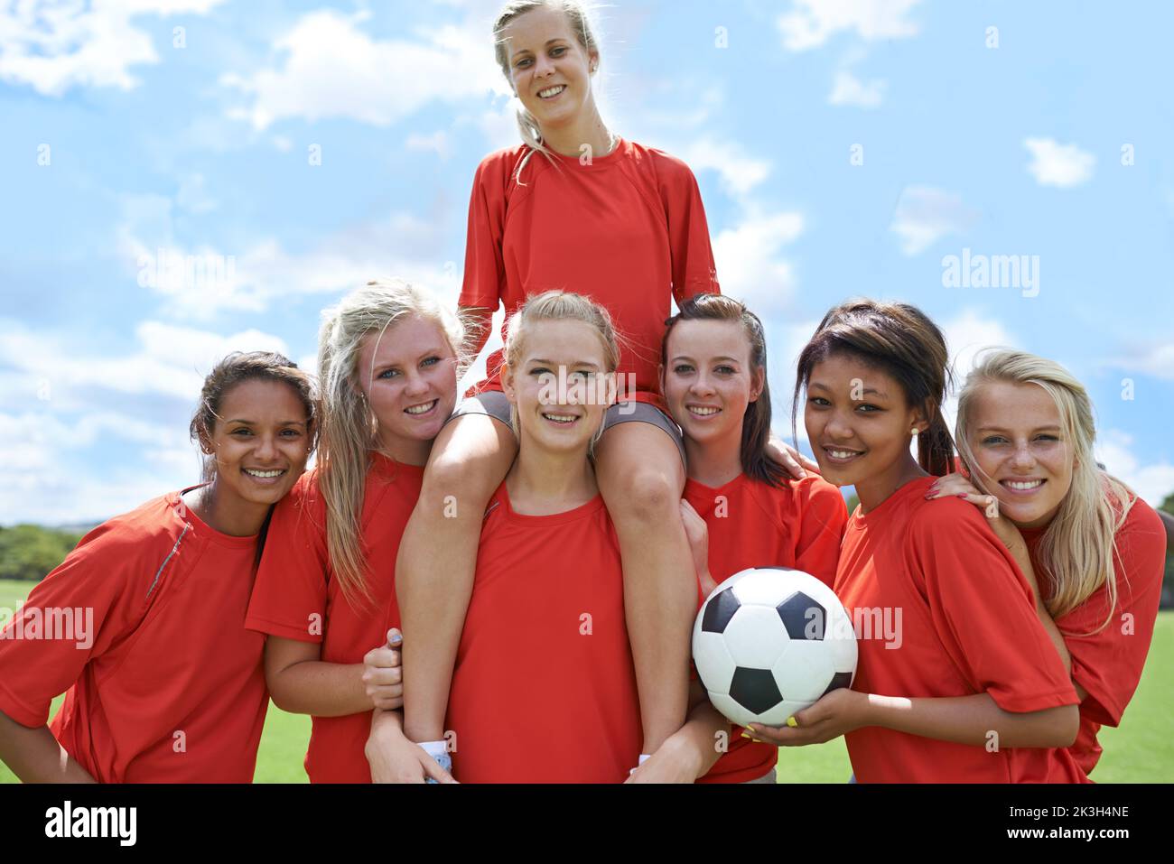 Vorteile für die Zukunft. Porträt einer Mädchenfußballmannschaft, die ihren Kapitän triumphierend aufhebt. Stockfoto