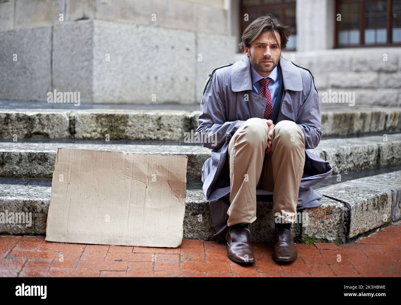 Will modellieren für Lebensmittel. Blick auf einen arbeitslosen Geschäftsmann, der auf den Stufen sitzt und um Arbeit bettelt. Stockfoto