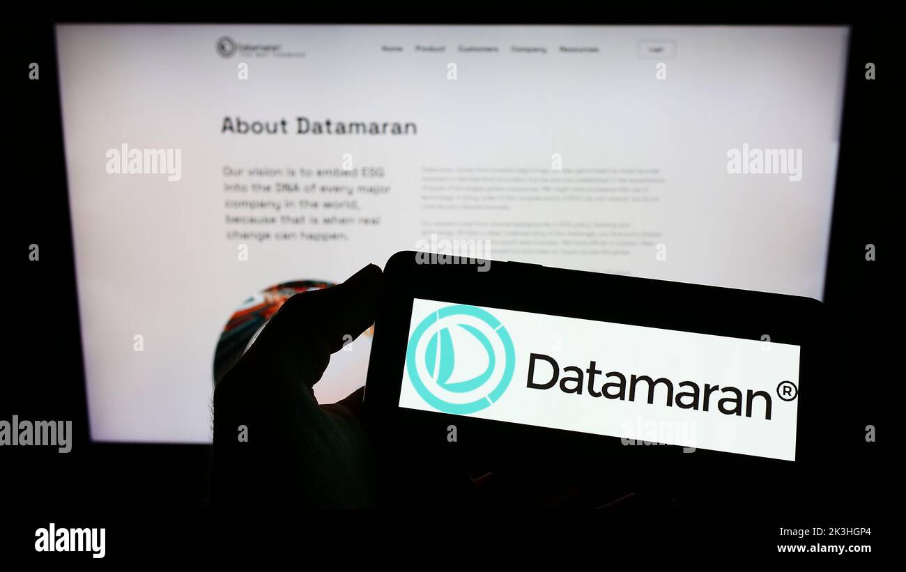 Person, die ein Mobiltelefon mit dem Logo des britischen Software-Unternehmens Datamaran Ltd. Auf dem Bildschirm vor der Webseite hält. Konzentrieren Sie sich auf die Telefonanzeige. Stockfoto