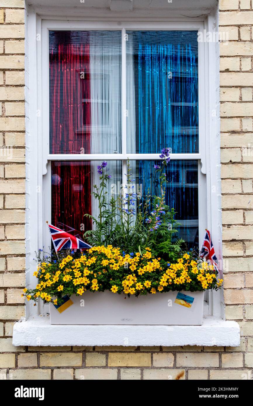 Eine Fensterbox mit gelben und blauen Fahnen in Solidarität mit der Ukraine und einem roten, weißen und blauen Vorhang und Gewerkschaftsjacken für das Queens Platinum Jubilee. Stockfoto