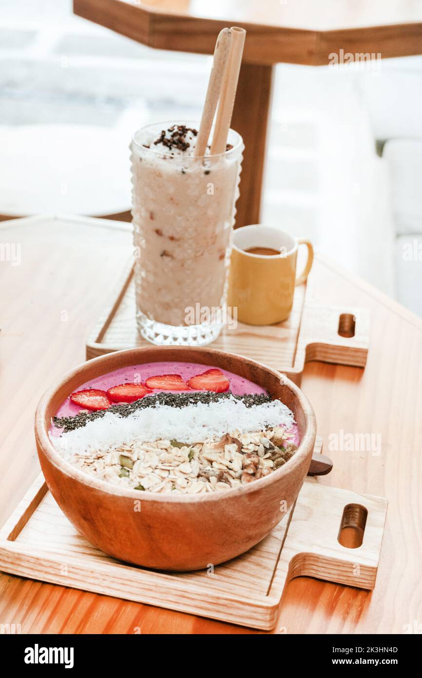 Köstliches gesundes Frühstück, Erdbeer-Smoothie-Schale mit Müsli, Früchten, Chiasamen und Kokosnuss, eine ästhetische Aufnahme auf hellem Hintergrund. Stockfoto