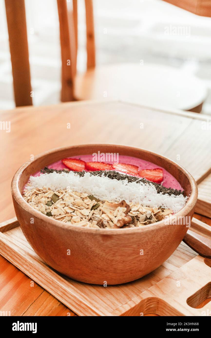 Köstliches gesundes Frühstück, Erdbeer-Smoothie-Schale mit Müsli, Früchten, Chiasamen und Kokosnuss, eine ästhetische Aufnahme auf hellem Hintergrund. Stockfoto