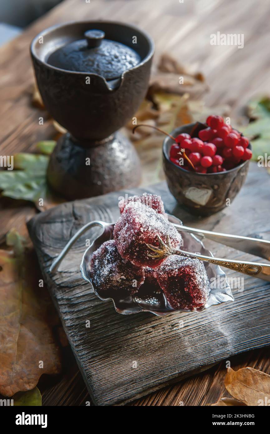 Fruchtmarmelade und chinesischer Tee in einem herbstlichen Stillleben. Original-Pinzette aus antikem Silber hält die Süßigkeiten. Stillleben im Herbst. Stockfoto