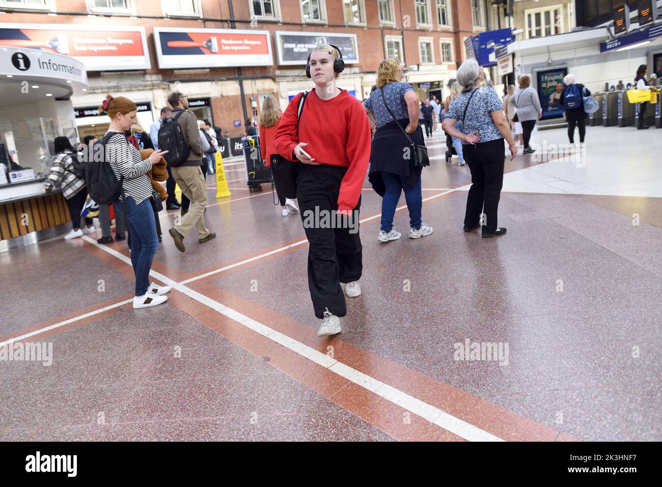 London, England, Großbritannien. Victoria Station: Junge Frau, die mit Telefon und Kopfhörern Musik hört Stockfoto