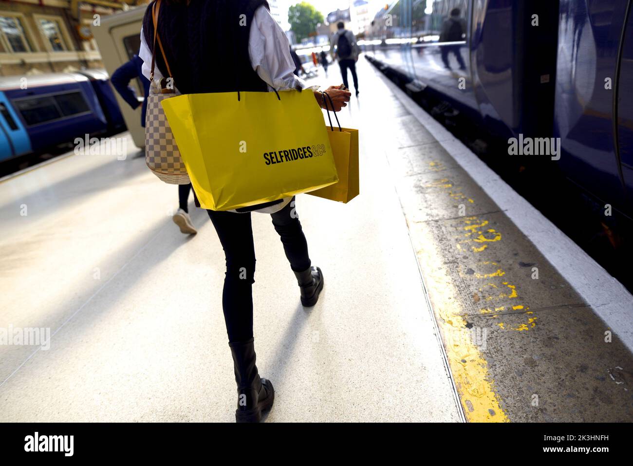 London, England, Großbritannien. Victoria Station - Frau auf der Plattform mit einem Selfridges-Beutel Stockfoto