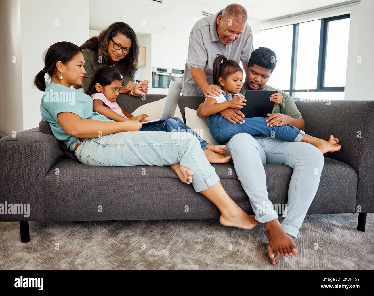 Familie, Kinder und Technik mit Kindern, Großeltern und Eltern im Wohnzimmer. Mädchen, Schwester und ältere Verwandte beobachten eine Stockfoto