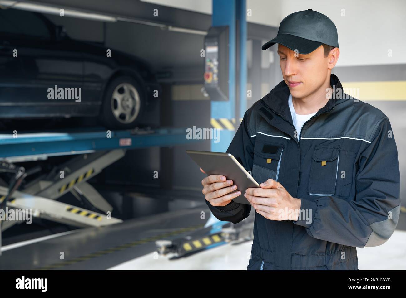 Servicearbeiter mit digitalem Tablet auf einem Hintergrund des Säulenlifters beim Autoservice Stockfoto