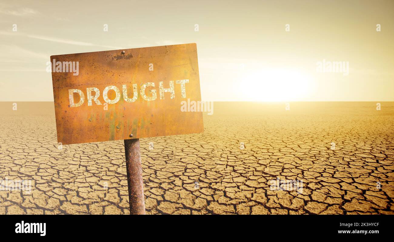 Ein rostiger Schild mit der Aufschrift DÜRRE auf dem Hintergrund einer Wüste mit rissigem Boden Stockfoto