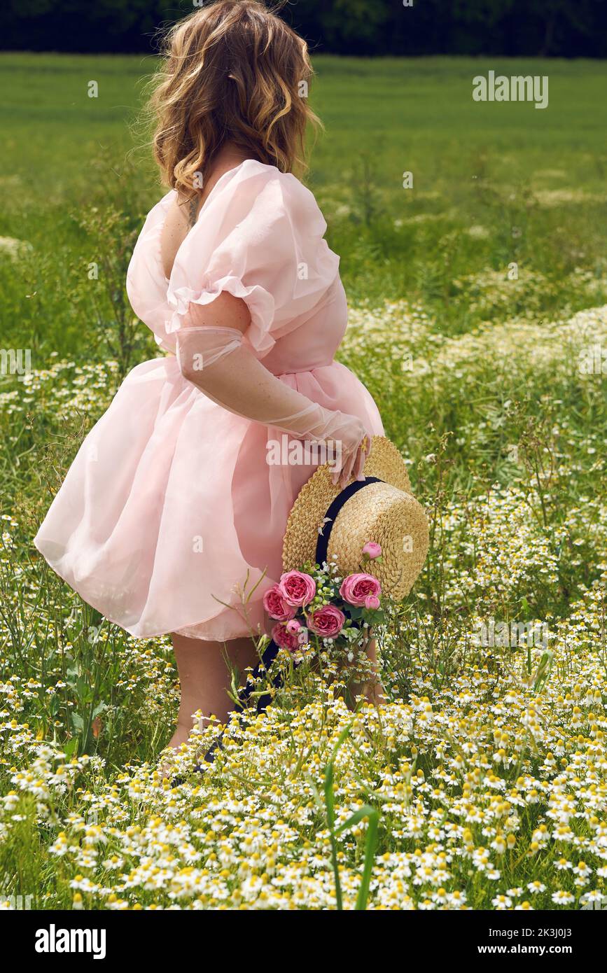 Im Sommer trägt eine junge blonde Frau in einem rosa geschwollenen Kleid auf einem Blumenfeld Stockfoto