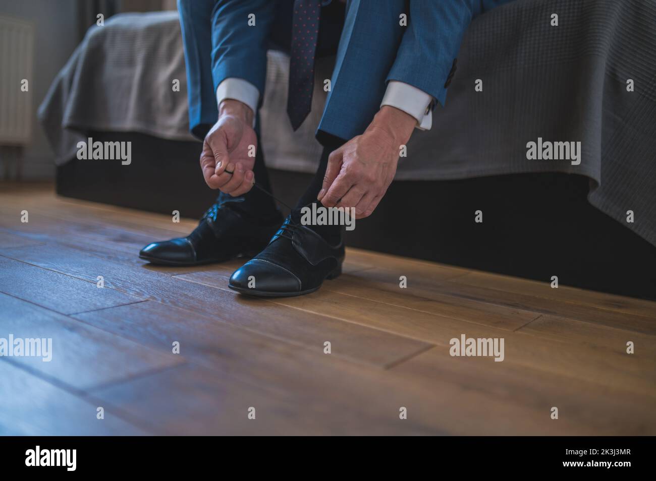 Mann in blauem Anzug, der seine Schuhe aufzieht, sitzt auf dem Sofa Stockfoto