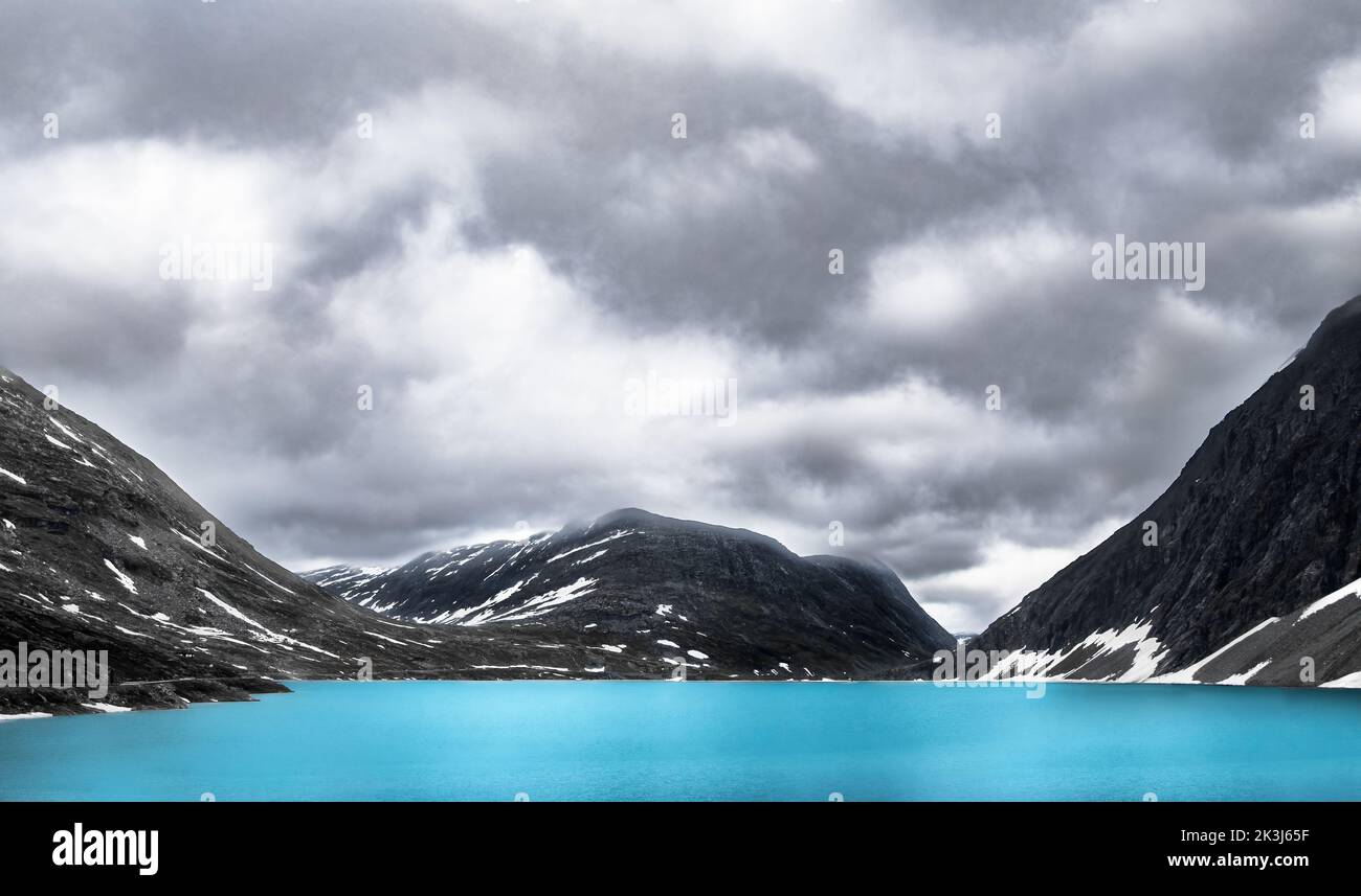 Ein türkisfarbener Schmelzwassersee in den norwegischen Bergen mit einem bewölkten Himmel und etwas Schnee, horizontal Stockfoto