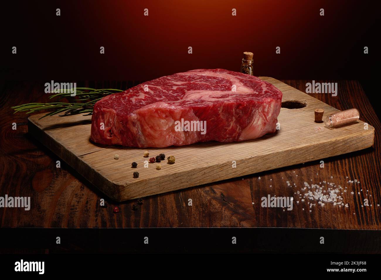 Marmoriertes Rindersteak mit himalaya-Salz, Gewürzen und grünem Rosmarin auf Schneidebrett auf dunklem Holztisch und warmem rustikalem Hintergrund Stockfoto
