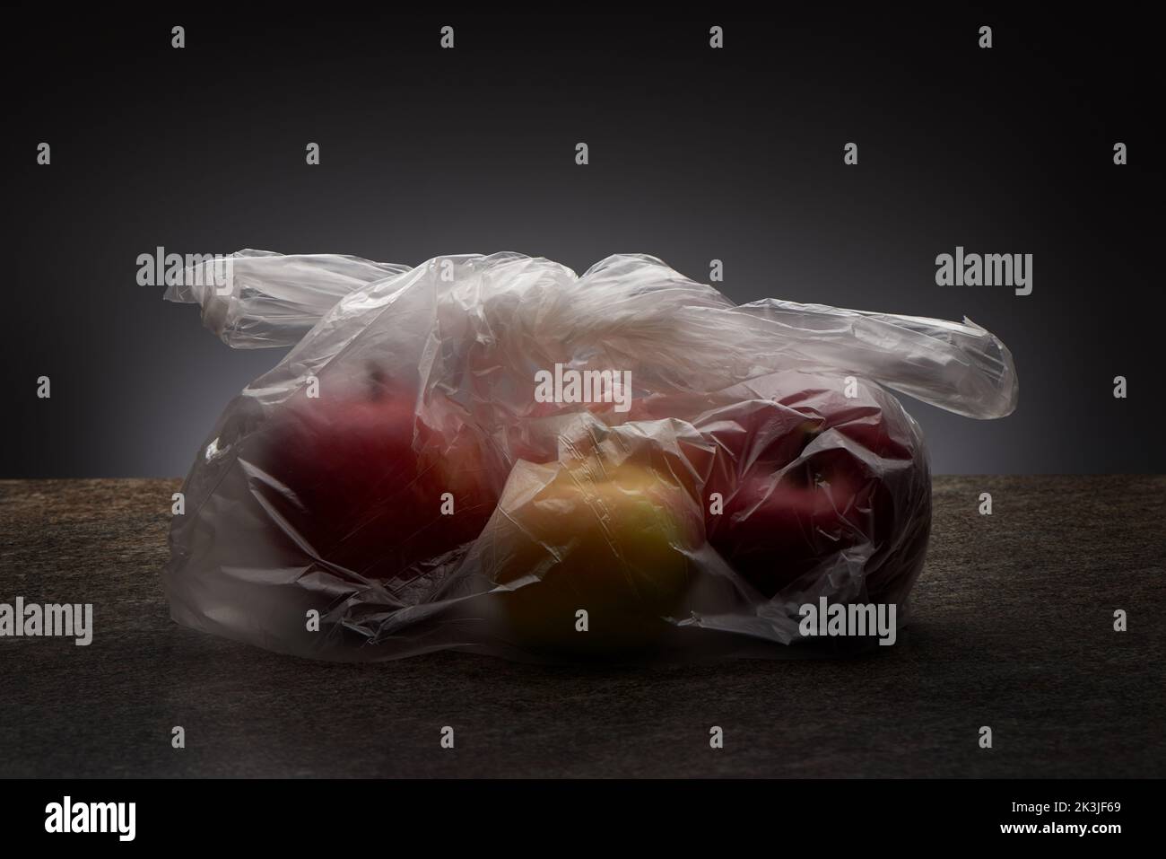 Rote und gelbe Bio-Äpfel in transparenter Plastiktüte auf Marmorplatte und grauem Hintergrund Stockfoto