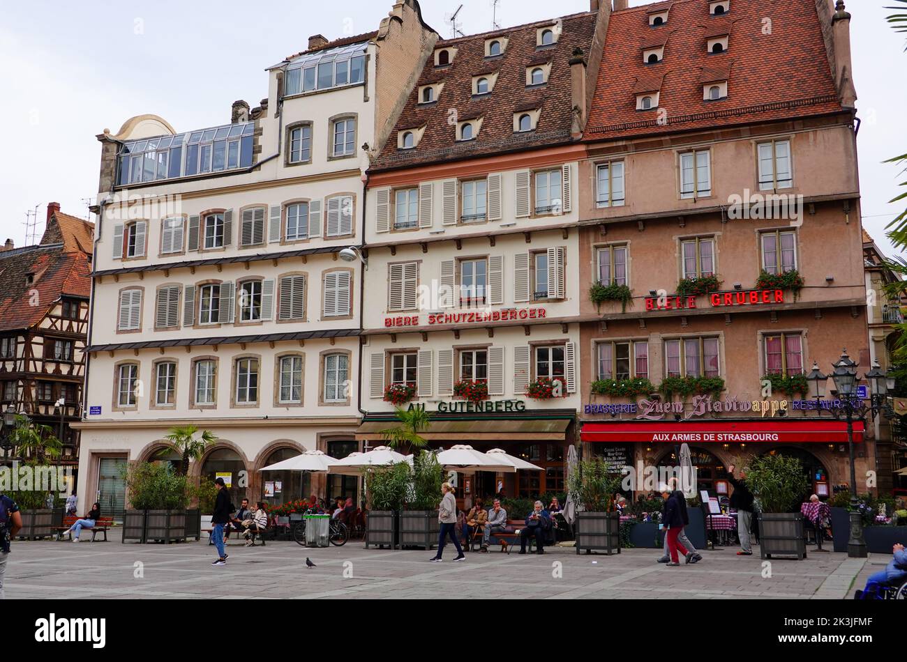 Menschen sitzen, zu Fuß, vor Gebäuden mit Architektur unverwechselbar der Region Elsass, Place Gutenberg, Straßburg, Frankreich. Stockfoto