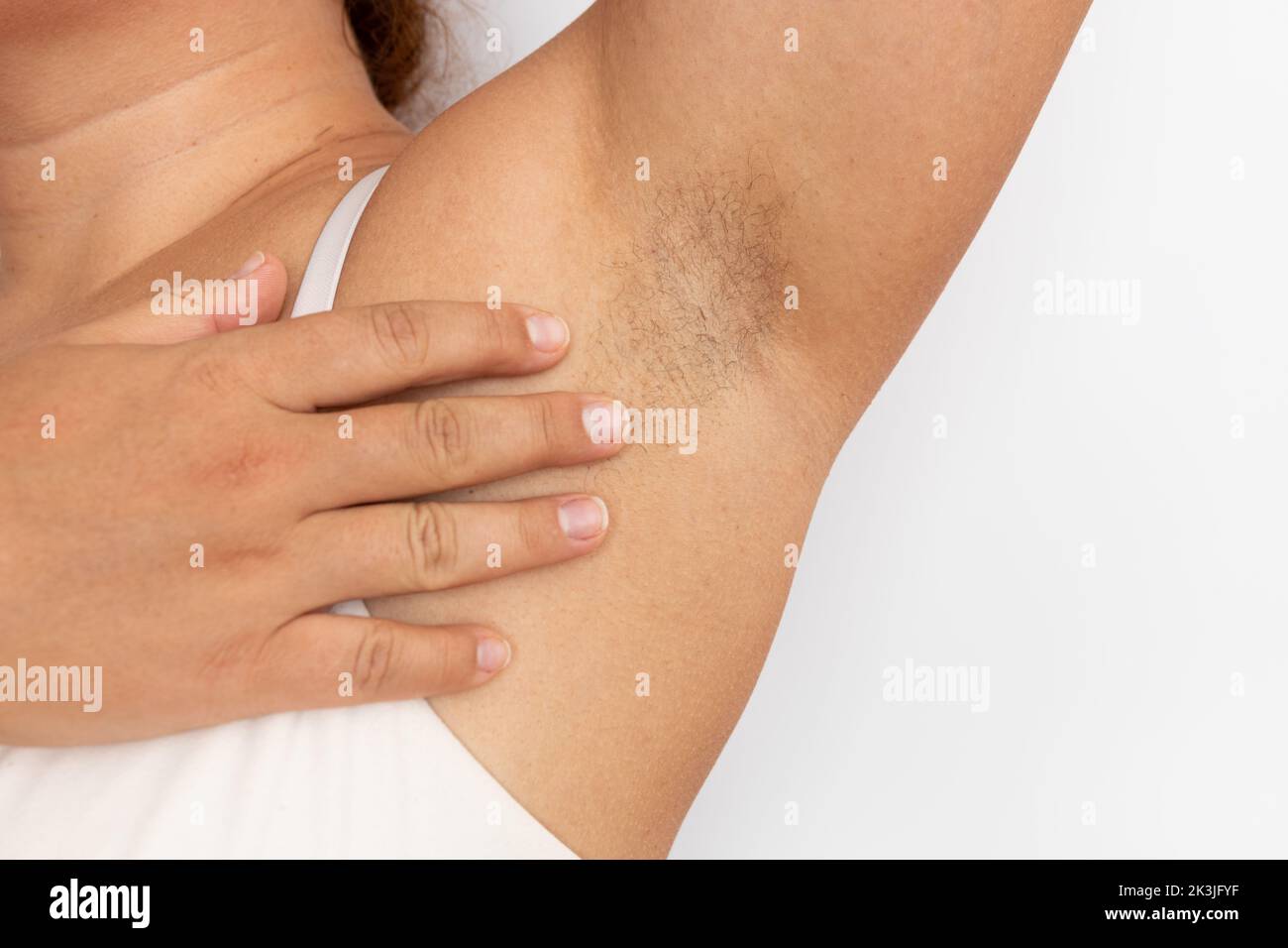 Frau berühren haarige Achselhöhlen mit Nahaufnahme der Hand, Freiraum für Kopien, beigefarbener Hintergrund. Angehobener Arm mit Achselhaaren. Weiblicher Beauty-Trend, Freiheit, Feminismus Stockfoto