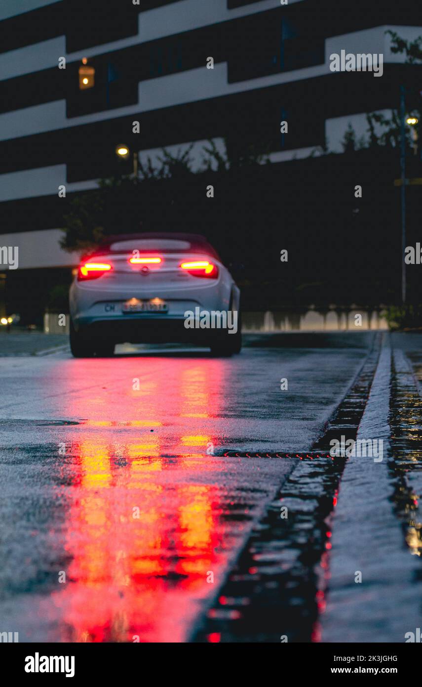 Autos Rücklicht reflektiert im Wasser / Regen auf dem Boden. Bordsteinkante dient als Richtlinie. Die Stimmung ist düster und das Bild sieht filmisch aus. Es ist Abend. Stockfoto