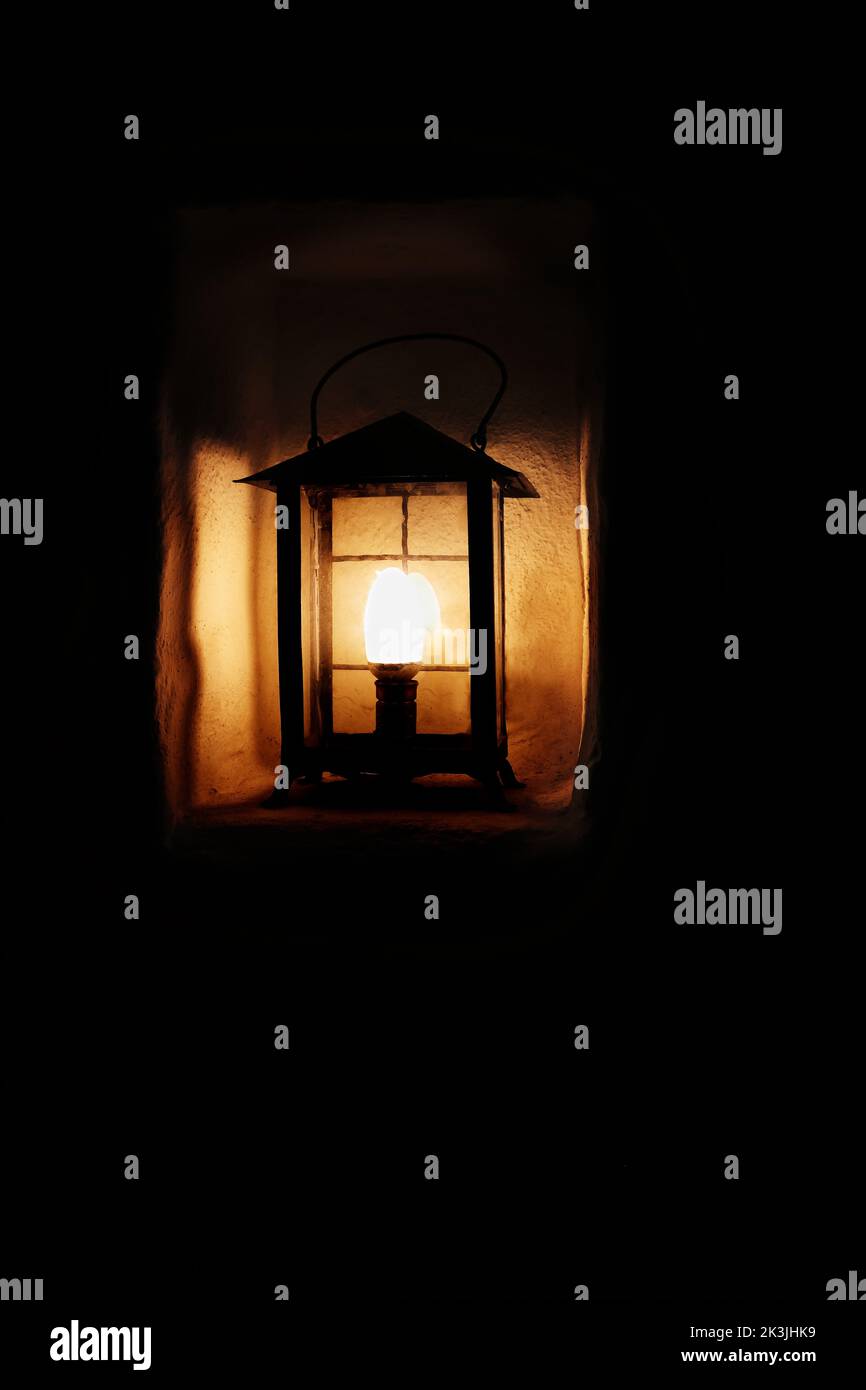 Alte Stahllaterne mit einer elektrischen Glühbirne in der Wandnische beleuchtet das alte Steinhaus. Dunkler Hintergrund. Alte weiße Steinmauer. Blurry ligh Stockfoto