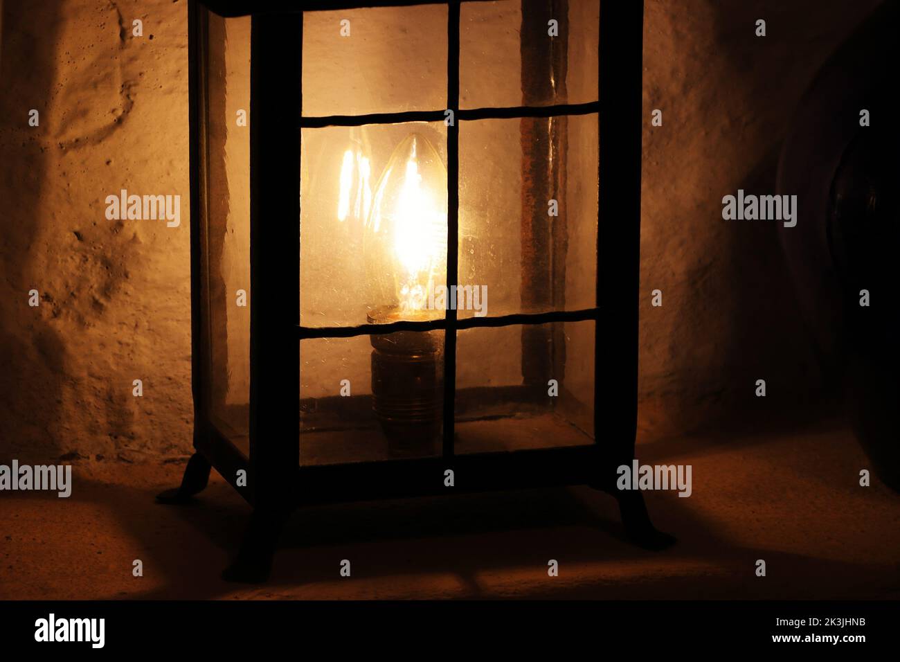Alte Stahllaterne mit einer elektrischen Glühbirne in der Wandnische beleuchtet das alte Steinhaus. Dunkler Hintergrund. Alte weiße Steinmauer. Blurry ligh Stockfoto