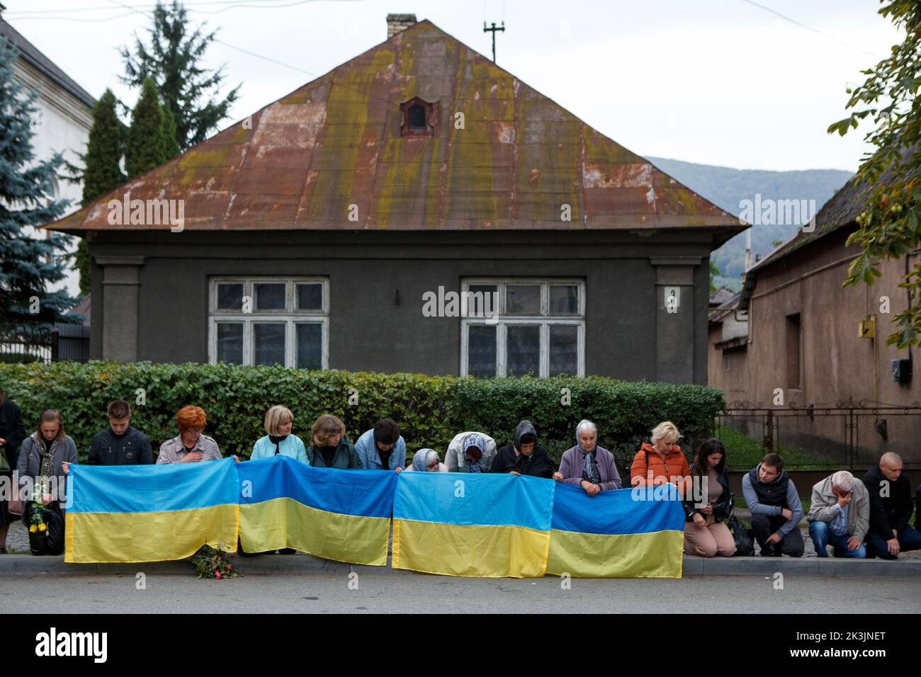 PERECHYN, UKRAINE - 25. SEPTEMBER 2022 - Menschen mit ukrainischen Flaggen knien, während die Autokolonne mit dem Leichnam von Oberleutnant Armen Petrosian, 50, Stockfoto