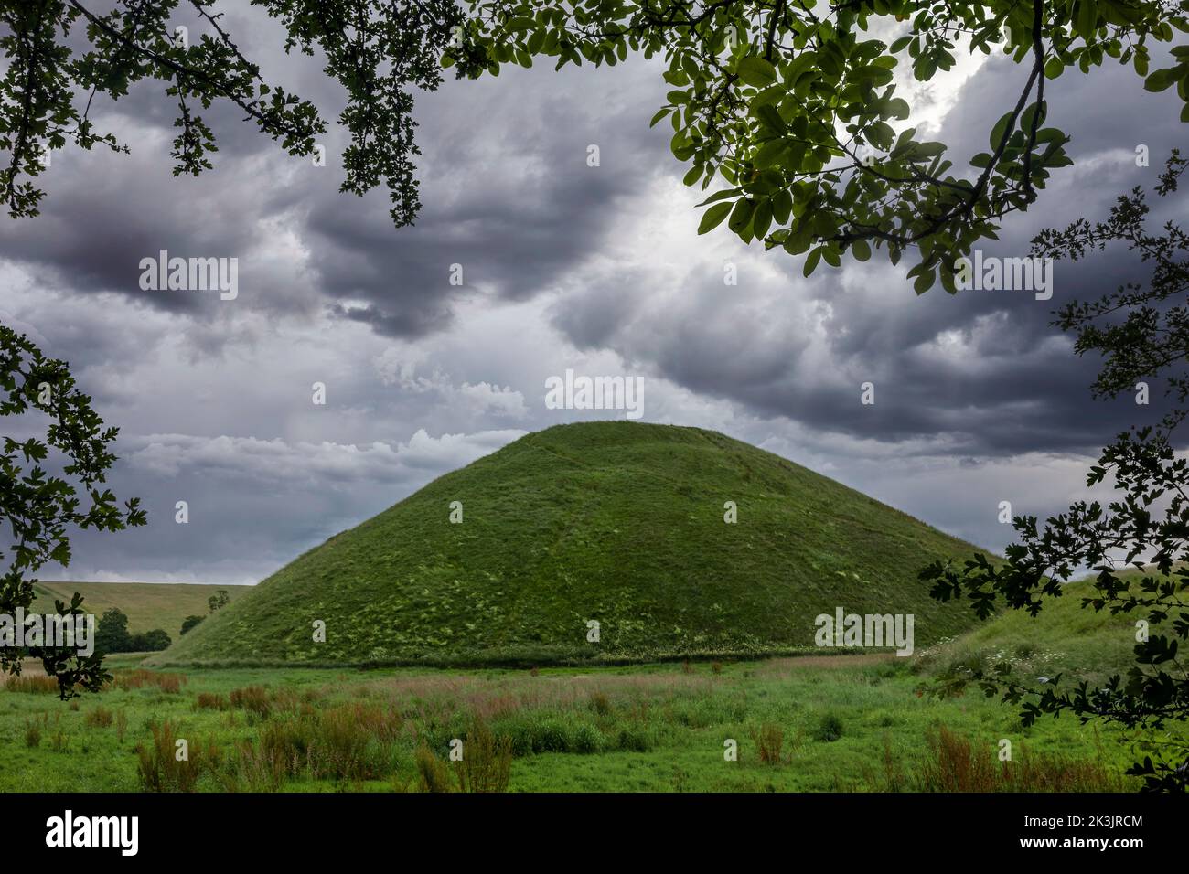 silbury Hill in der Nähe von avebury wiltshire durch einen Rahmen von Bäumen mit dramatischen Wolken gesehen Stockfoto