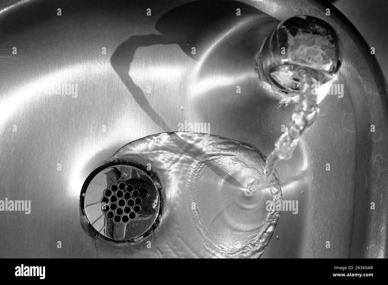 Glänzendes Waschbecken aus Stahl mit Wasser, das den Abfluss hinunterfließt Stockfoto