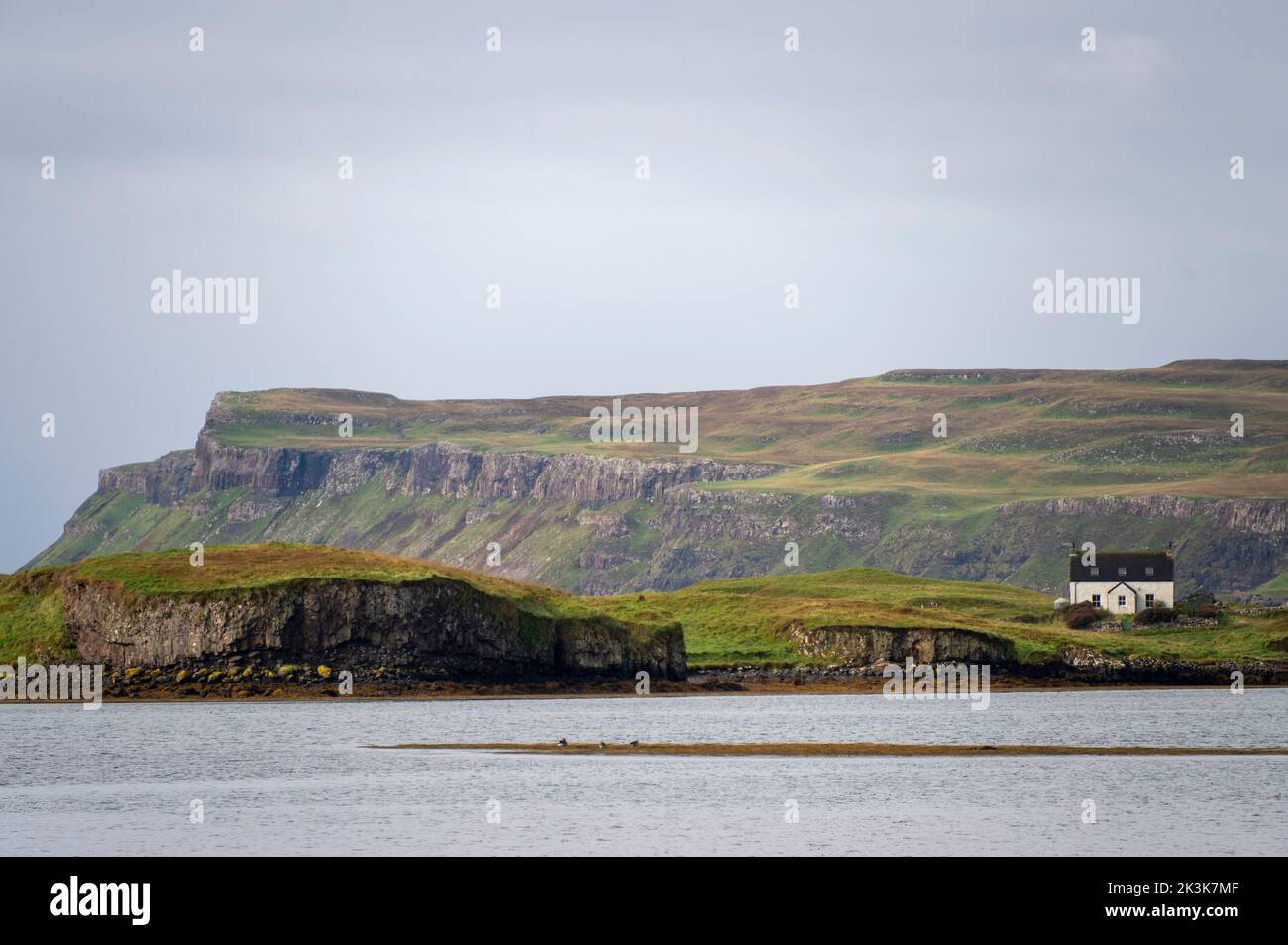 September 2022: Isle of Canna, Inner Hebrides, Schottland Ein kleines Haus mit den Klippen von Canna im Hintergrund Stockfoto