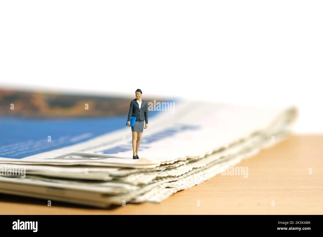 Miniatur Menschen Spielzeug Figur Fotografie. Eine Geschäftsfrau, die mit einer Zeitung auf dem Schreibtisch herumläuft. Isoliert auf weißem Hintergrund. Bildfoto Stockfoto