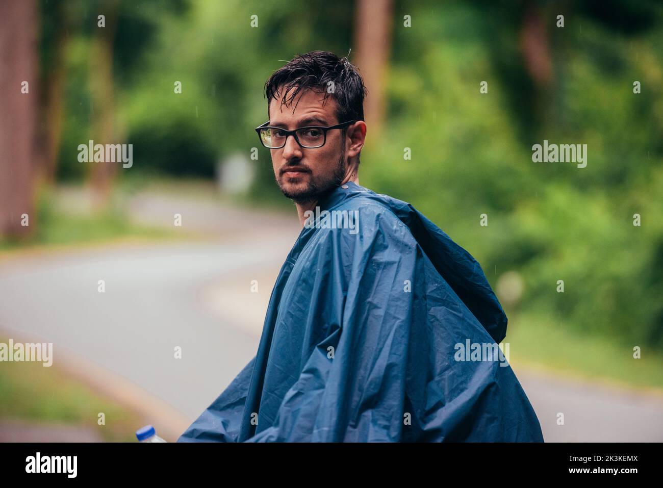 Mann mit Regenmantel in der Mitte einer Straße neben dem Wald Stockfoto
