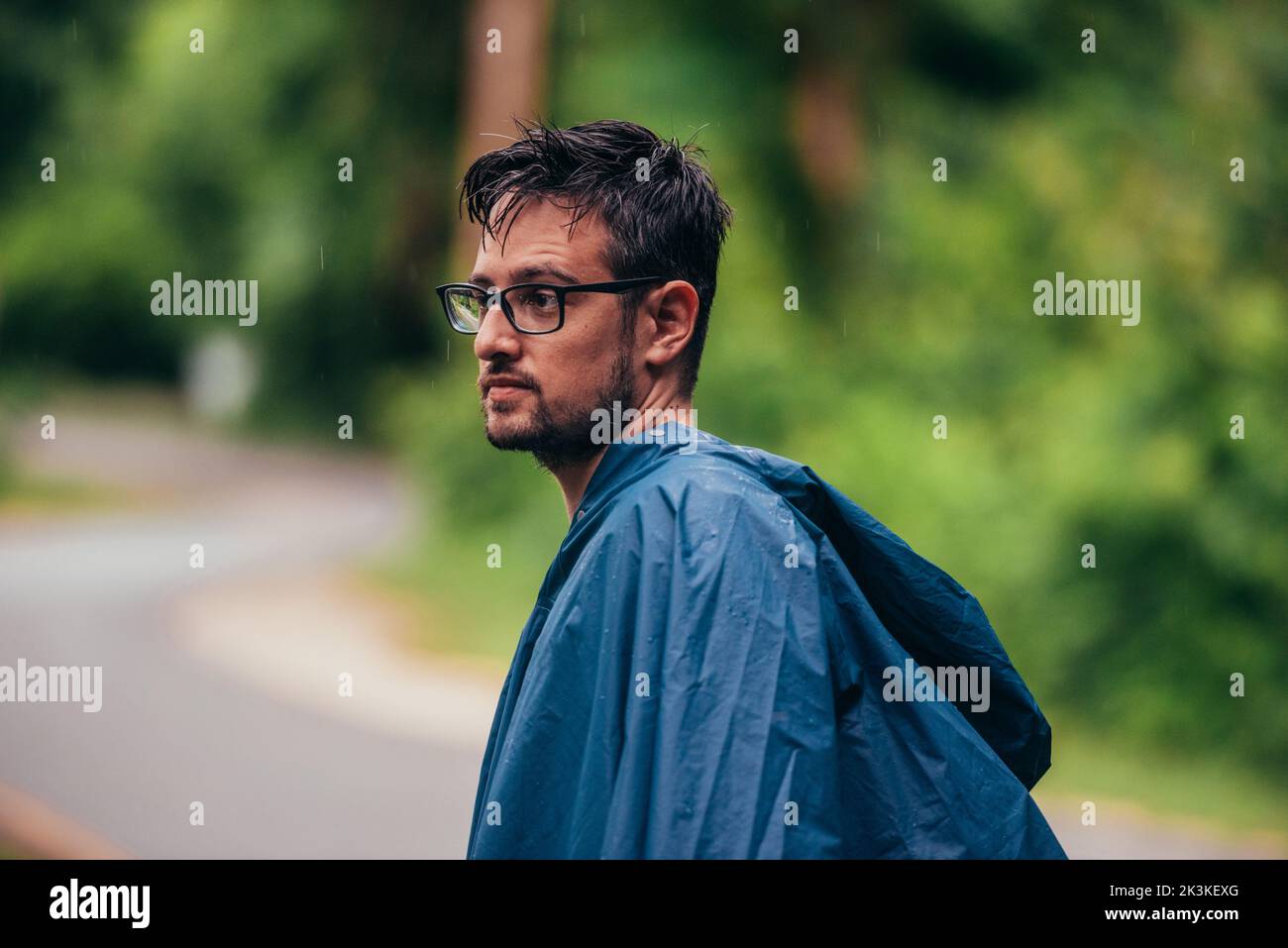 Mann mit Regenmantel in der Mitte einer Straße neben dem Wald Stockfoto