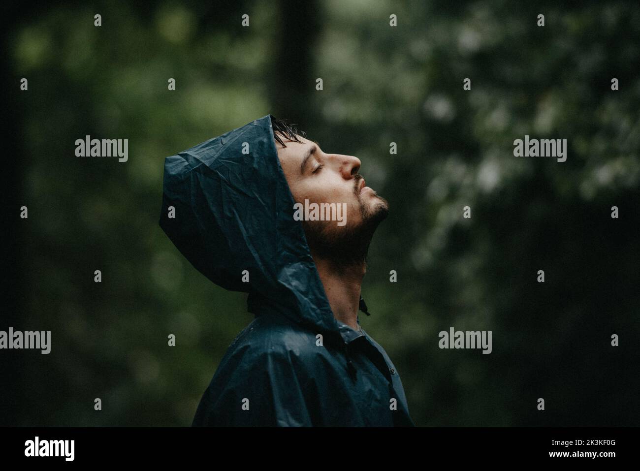 Mann mit geschlossenen Augen, in einem Regenmantel, mitten in einem Wald Stockfoto