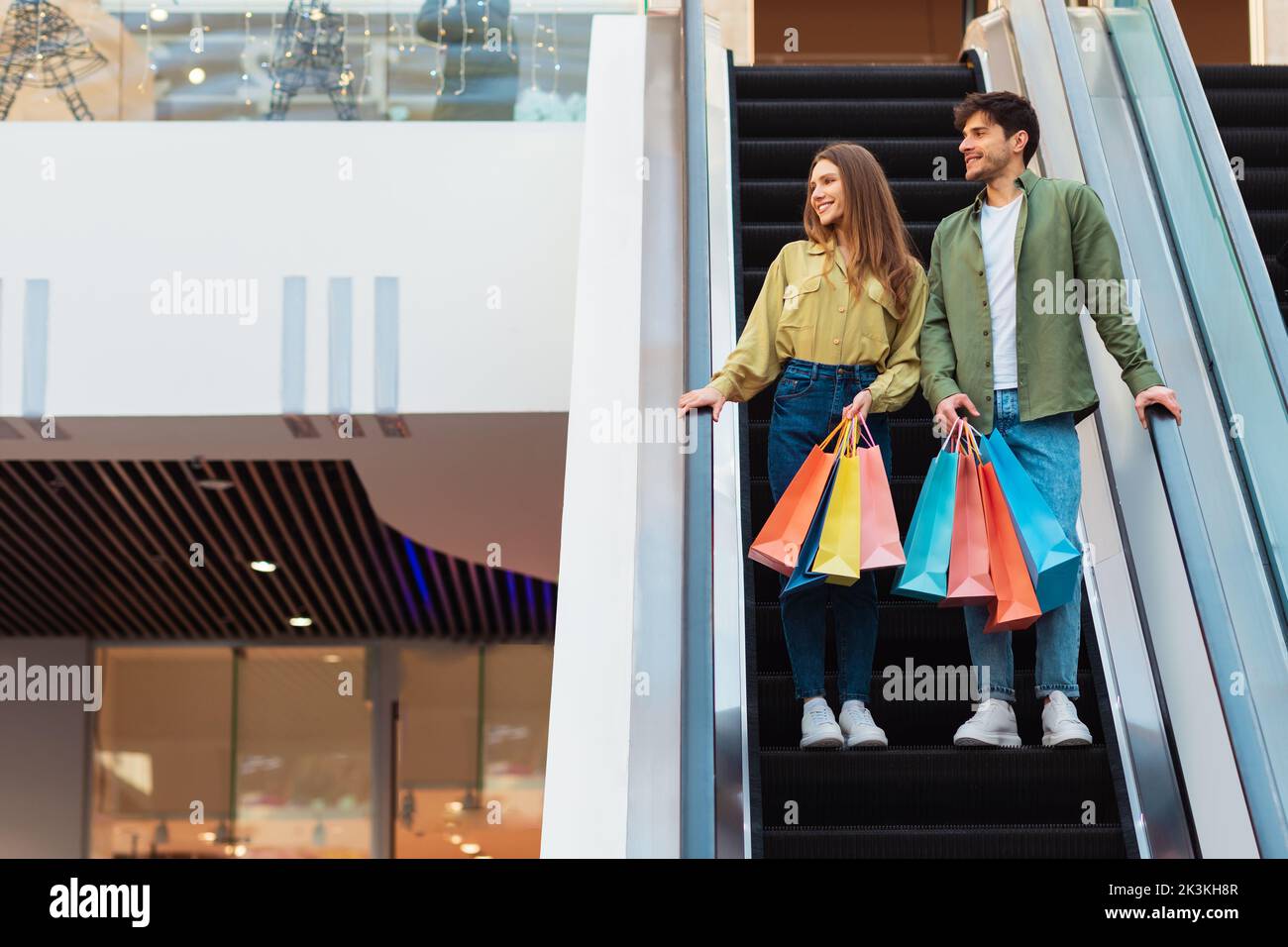 Ehepartner Stehen Auf Beweglichen Treppen Und Halten Einkaufstaschen Im Hypermarket Stockfoto