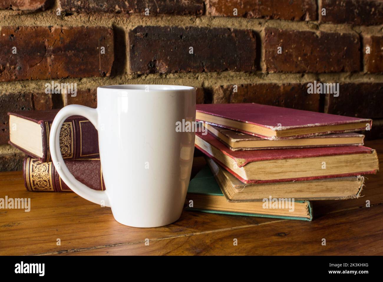 Ein Stapel alter, gut gelesenen Bücher zusammen mit einem großen weißen Kaffeebecher. Stockfoto