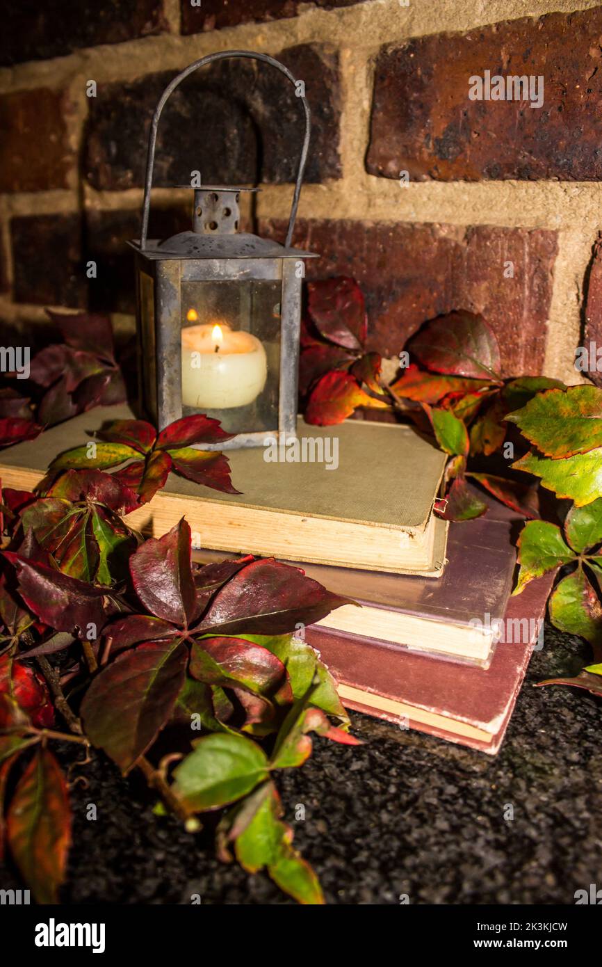 Rustikales Stillleben eines Stapels alter Bücher und eines Laterne-förmigen Kerzenhalters Stockfoto
