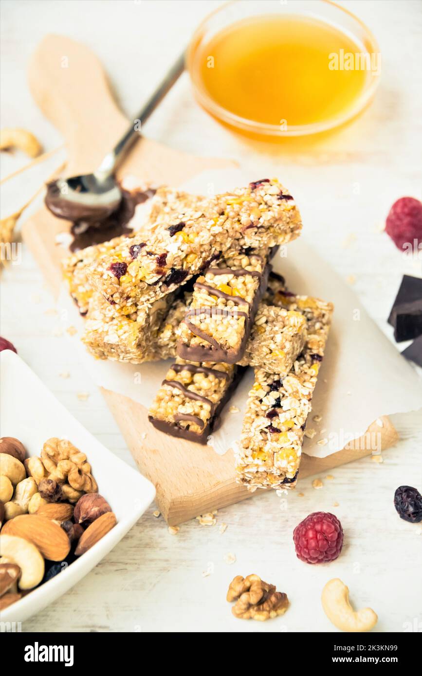 Verschiedene hausgemachte Müsliriegel mit Nüssen, Samen, dunkler Schokolade, Honig und Beeren auf einem Holzbrett. Stockfoto