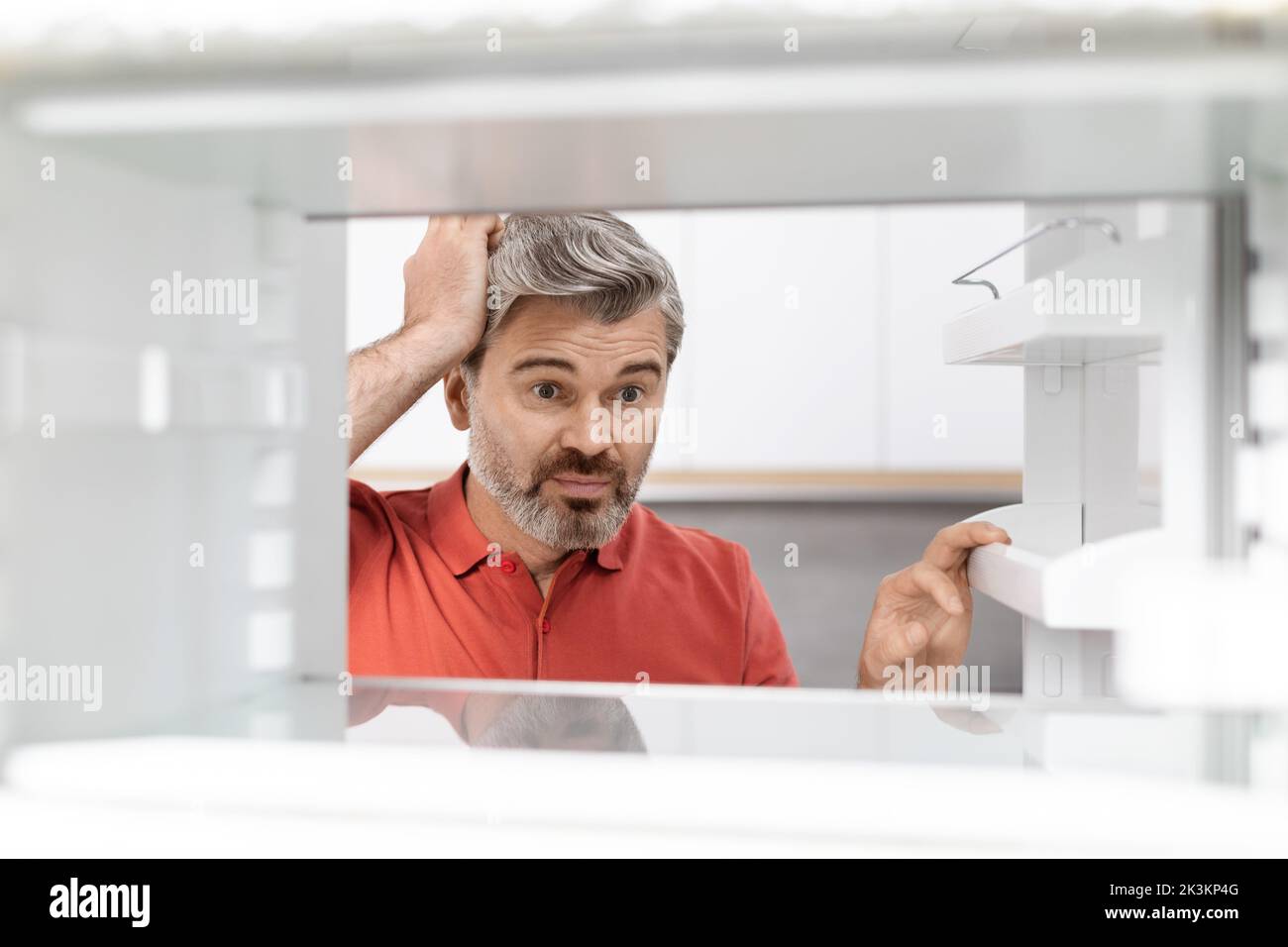 Überfordert Mann mittleren Alters, der in einen leeren Kühlschrank schaute Stockfoto