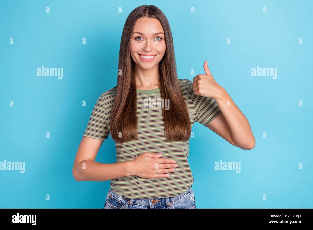 Portrait Foto von jungen positiven attraktiven Mädchen zeigt Daumen nach oben wie gute Laune halten Hand Bauch pms gesunde Ernährung isoliert auf blauem Hintergrund Stockfoto